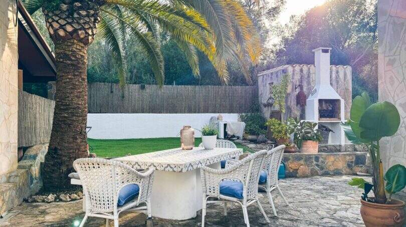 Gepflegter Außenbereich mit weißen Rattanmöbeln, Palme und Grillkamin in Cala Murada