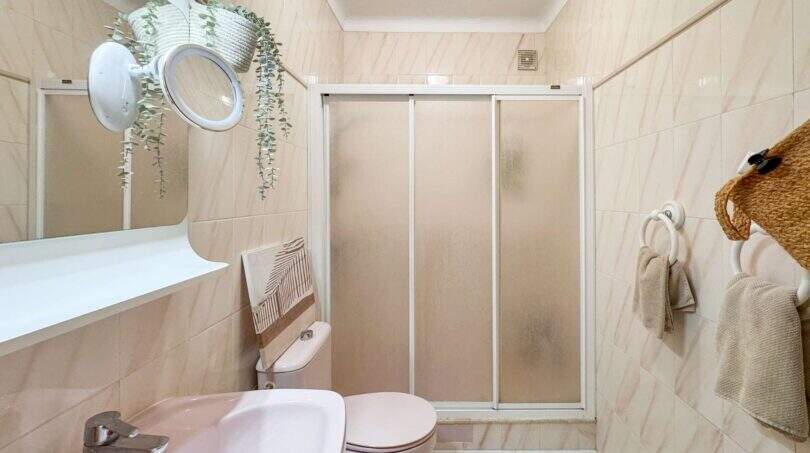 Helles Badezimmer mit Duschkabine, WC, Waschbecken und Pflanzendekor in der Strandwohnung Cala Murada