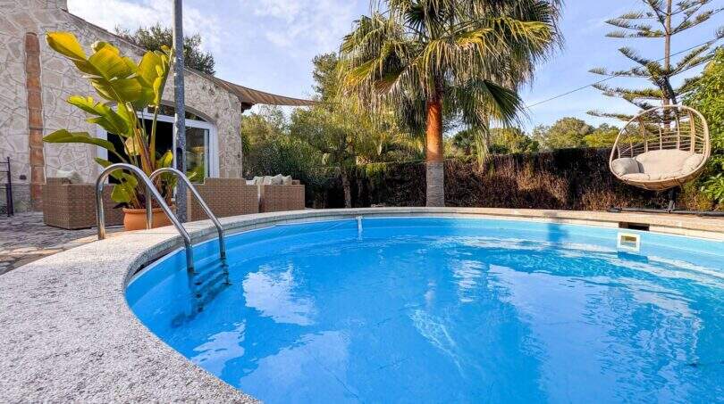 Runder Pool mit Metallleiter, Palmen, Hängesessel und Natursteinhaus in Cala Murada
