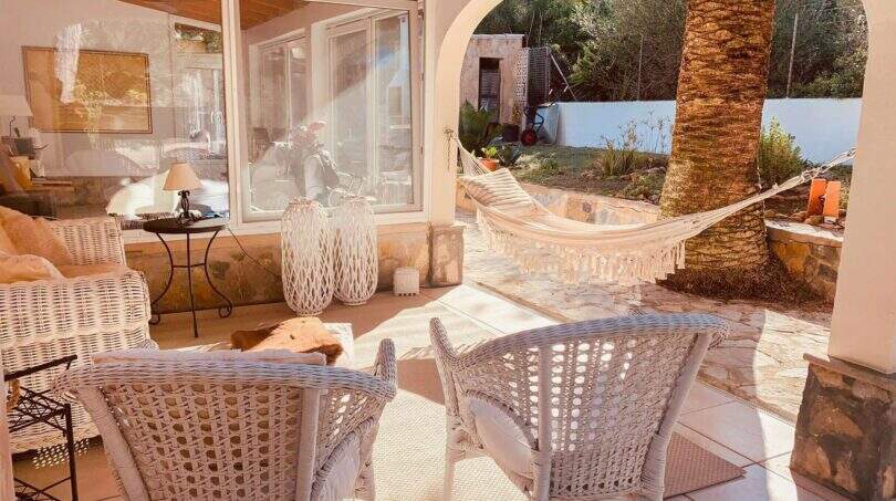 Überdachte Terrasse mit weißen Rattanmöbeln, Hängematte und Palme in Cala Murada