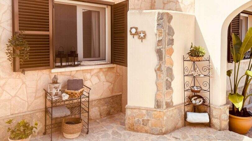 Mediterraner Außenbereich mit Natursteinwand, Holzfensterläden und dekorativen Regalen in Cala Murada