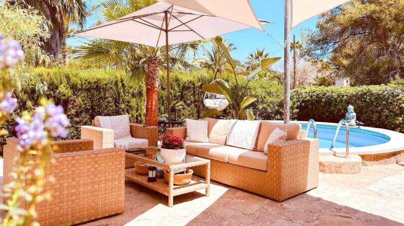 Sonnige Terrasse mit Rattanmöbeln, Sonnenschirm und Pool, umgeben von Palmen – Wohlfühloase in Cala Murada