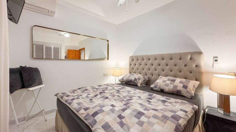 Helles Schlafzimmer mit Doppelbett, gepolstertem Kopfteil, Wandspiegel und Klimaanlage in Cala Murada