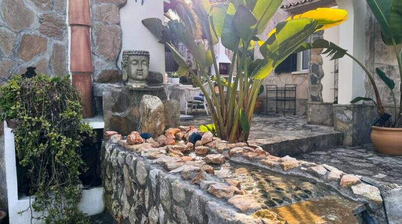 Mediterraner Innenhof mit Buddha-Brunnen, Natursteinmauern und tropischen Pflanzen in der Wohlfühloase Cala Murada