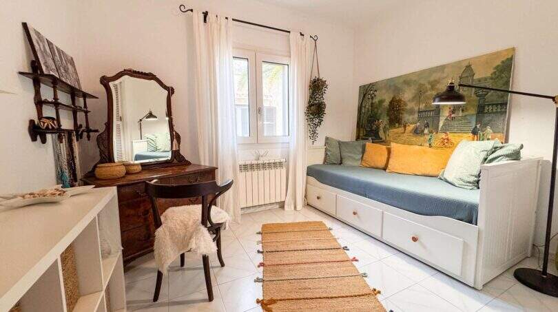 Helles Schlafzimmer mit antikem Schminktisch, weißem Tagesbett, Gemälde und Naturrugs in Cala Murada