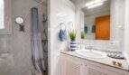 Helles Badezimmer mit Marmoroptik, Dusche, Waschtisch und blauer Deko in der Strandwohnung Cala Murada