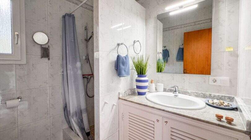 Helles Badezimmer mit Marmoroptik, Dusche, Waschtisch und blauer Deko in der Strandwohnung Cala Murada