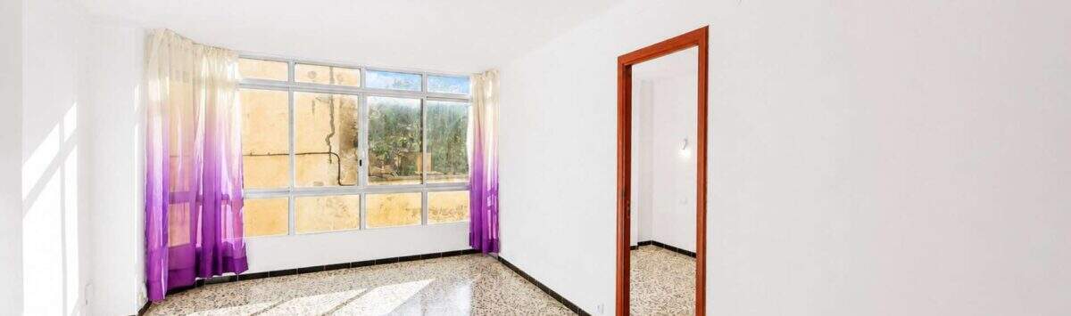 Leeres Wohnzimmer mit Terrazzoboden, lila Vorhängen und großem Fenster in Felanitx