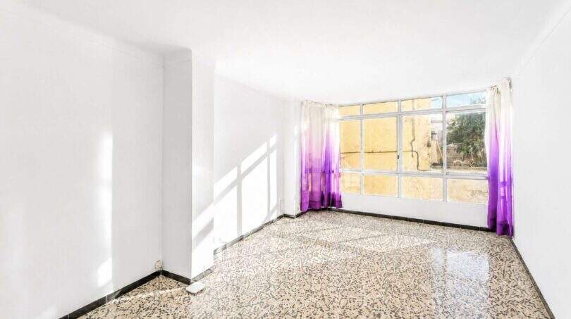 Leeres Wohnzimmer mit Terrazzoböden, weißen Wänden und großem Fenster mit lila Vorhängen in Felanitx