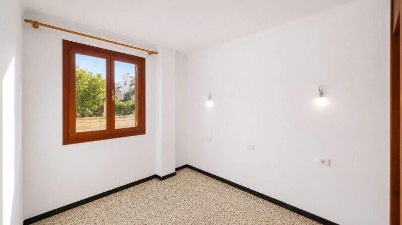 Leeres Schlafzimmer mit Terrazzoboden, Holzfenster und Gartenblick in einem Wohnhaus in Felanitx