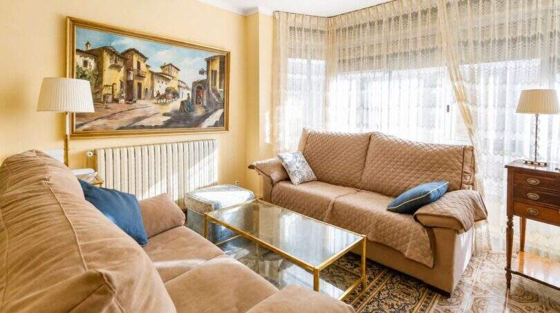 Helles Wohnzimmer in Felanitx mit zwei Sofas, Glastisch, Gemälde und großem Fenster mit Spitzengardinen.
