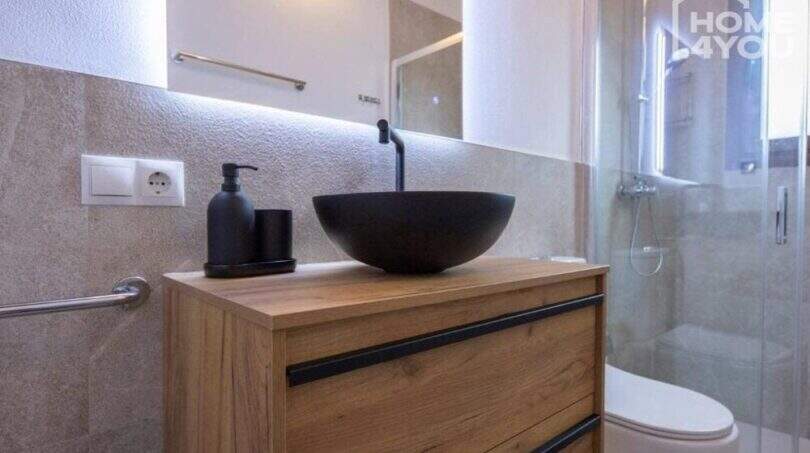 Modernes Bad mit schwarzem Aufsatzwaschbecken, Holzwaschtisch, Glasdusche und WC im Bungalow Alcúdia.