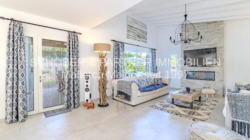 Helles Wohnzimmer der mediterranen Villa in Sa Coma mit Steinwand, Kamin, Sofa und Terrassenzugang.