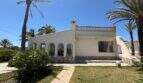 Mediterrane Villa in Cala Murada mit weißer Fassade, Bogenfenstern, Balustrade und Palmen im gepflegten Garten.