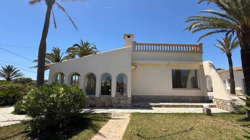 Mediterrane Villa in Cala Murada mit weißer Fassade, Bogenfenstern, Balustrade und Palmen im gepflegten Garten.