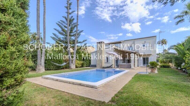Mediterrane Villa in Sa Coma mit pool, gepflegtem Garten und Palmen unter blauem Himmel.