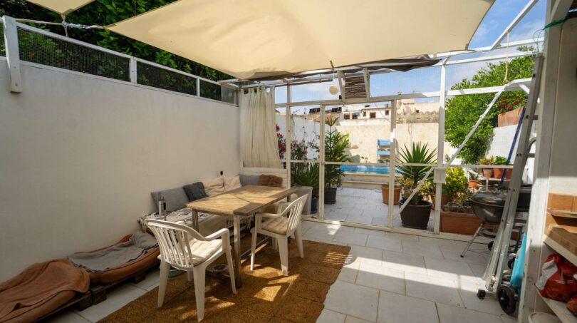 Terraza cubierta con mesa de comedor, área lounge y vista a piscina y jardín de una casa multifamiliar en Felanitx.