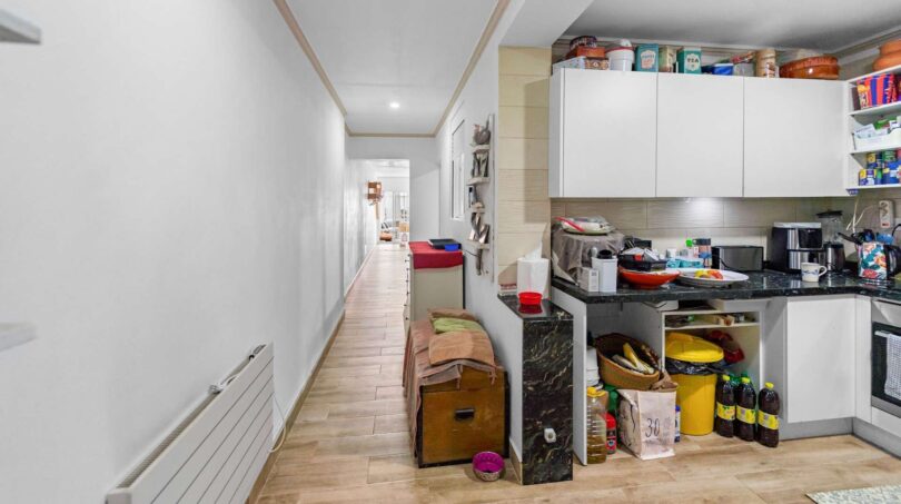 Pasillo estrecho con piso de madera y cocina blanca con encimera oscura en casa multifamiliar alquilable, Felanitx