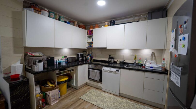 Cocina empotrada moderna con frentes blancos, encimera de granito, lavavajillas y estufa en unidad de vivienda alquilada, Felanitx