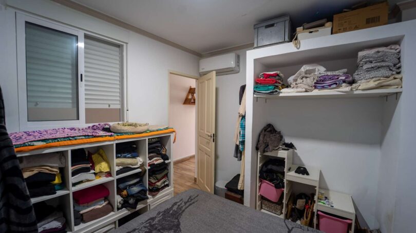 Vestidor con estantes abiertos llenos de ropa, aire acondicionado y ventana en casa unifamiliar en Felanitx.