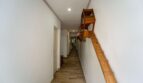 Pasillo largo con piso de madera, paredes blancas y escalera de madera al piso superior en casa multifamiliar Felanitx