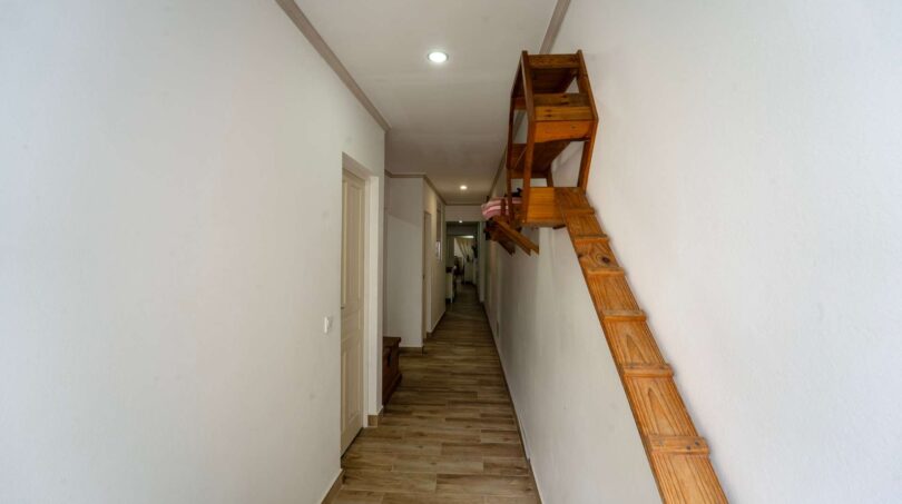 Pasillo largo con piso de madera, paredes blancas y escalera de madera al piso superior en casa multifamiliar Felanitx
