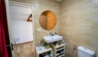 Baño con espejo redondo, lavabo y azulejos de piedra claros en casa unifamiliar alquilada en Felanitx