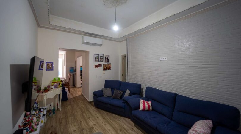 Sala de estar con sofá azul, pared de ladrillo blanco y aire acondicionado en unidad residencial alquilada en Felanitx