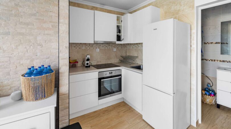 Moderna cocina empotrada blanca con revestimiento de pared de piedra, horno y frigorífico en casa de múltiples familias Felanitx
