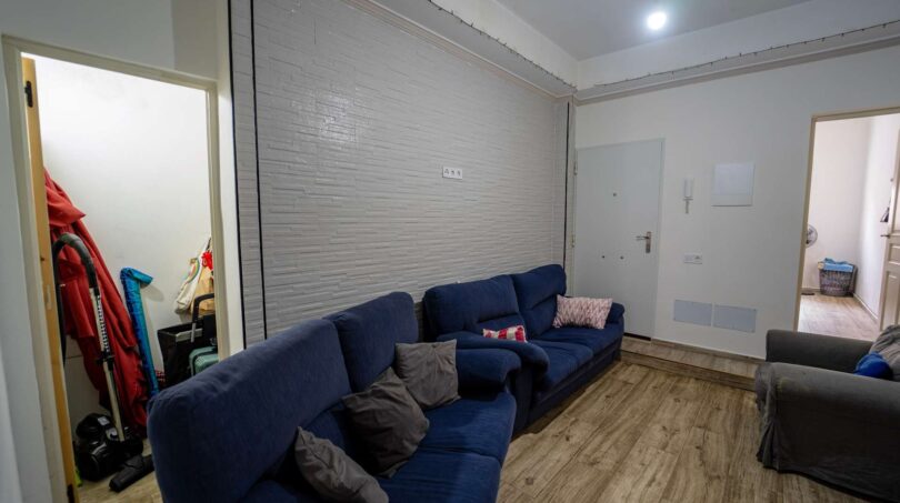 Sala de estar con sofá esquinero azul, suelo de madera y pared de piedra en casa unifamiliar alquilada en Felanitx