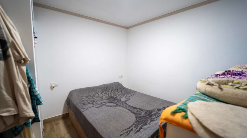 Pequeño dormitorio con cama doble, manta de árbol gris y piso laminado en unidad de vivienda alquilada, Felanitx