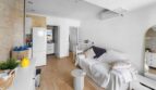 Luminosa sala de estar con sofá blanco, suelo de madera y cocina abierta en casa de múltiples familias Felanitx