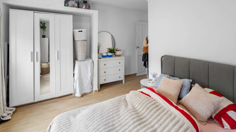Luminoso dormitorio con armario blanco, cómoda, espejo redondo y acogedora cama doble en casa unifamiliar Felanitx