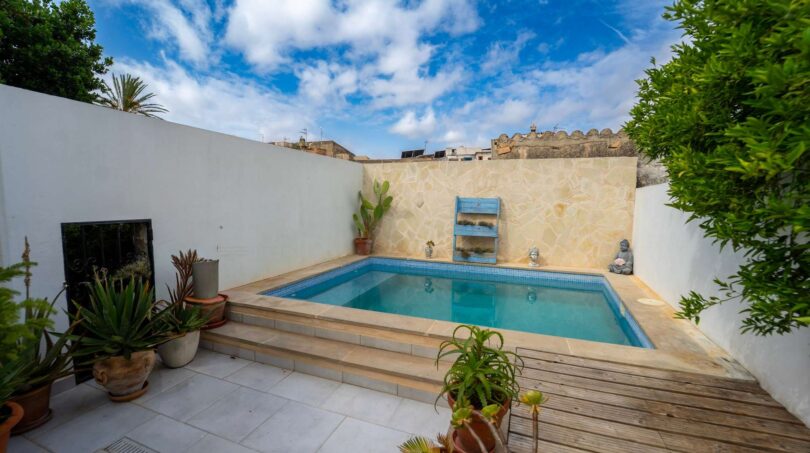 Pequeña piscina exterior con pared de piedra natural, terraza de madera y plantas mediterráneas en el patio interior de la casa unifamiliar en Felanitx.