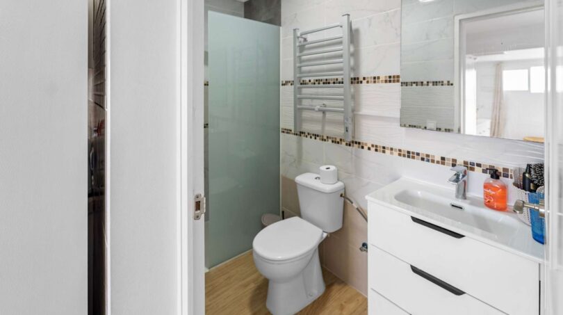 Baño luminoso con ducha, inodoro y lavamanos blanco en unidad residencial alquilada, Felanitx