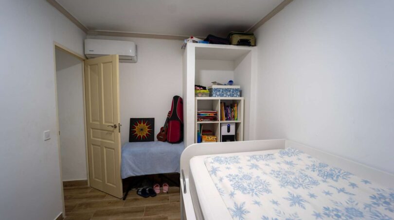 Dormitorio con cama individual, estantería, aire acondicionado y guitarra en casa unifamiliar alquilada en Felanitx.