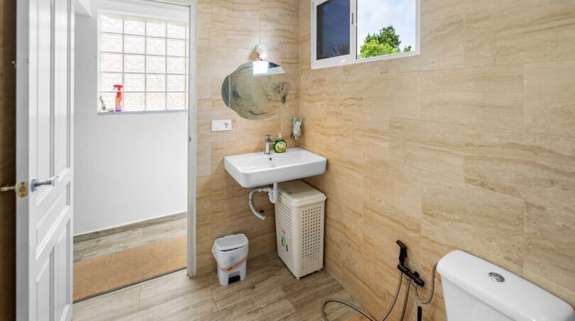 Baño luminoso con lavamanos, inodoro y azulejos beige en casa unifamiliar alquilada en Felanitx.