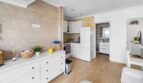 Cocina-comedor abierta con armarios blancos, revestimiento de pared de piedra y suelo de madera en casa unifamiliar alquilada en Felanitx.