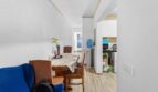 Estrecho comedor-sala con mesa de madera, sofá azul, hervidor y vista a la cocina moderna, Felanitx