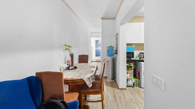 Estrecho comedor-sala con mesa de madera, sofá azul, hervidor y vista a la cocina moderna, Felanitx