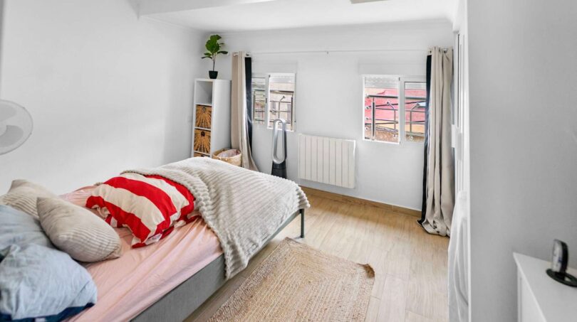 Luminoso dormitorio con cama doble, suelo de madera, dos ventanas y paredes blancas en casa de múltiples familias en Felanitx.