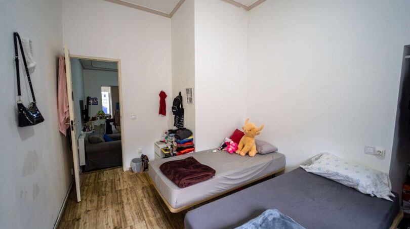Dormitorio con dos camas individuales, suelo de madera y paso a la zona de estar en unidad alquilada en Felanitx.