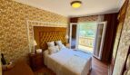Bedroom of the retro villa in Porto Cristo with upholstered headboard, gold wallpaper and balcony with garden view.
