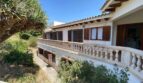 Exterior view of the retro villa in Porto Cristo with balustrade, wooden shutters and lush greenery.
