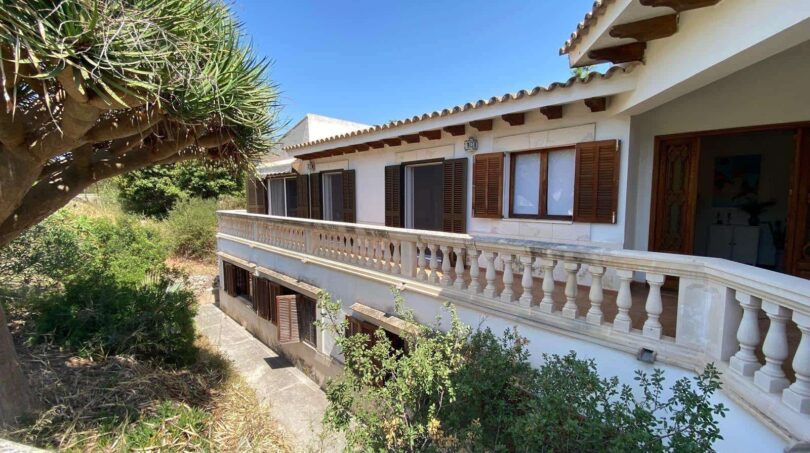 Exterior view of the retro villa in Porto Cristo with balustrade, wooden shutters and lush greenery.