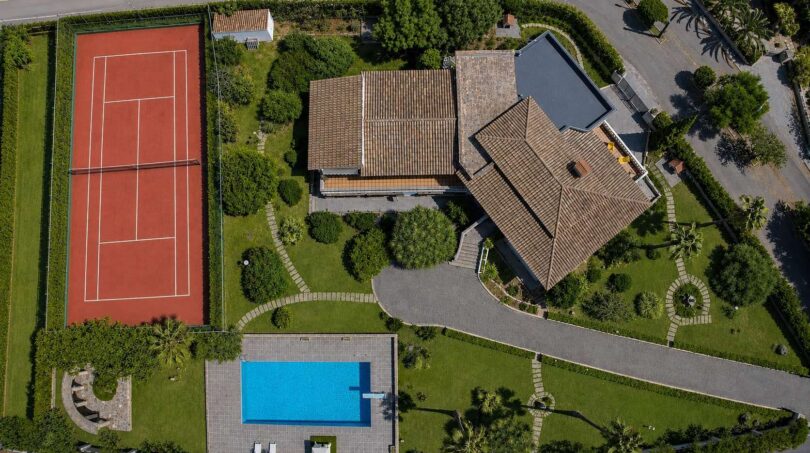 Aerial view of the villa in Porto Cristo with tennis court, pool, manicured garden and terracotta roof.