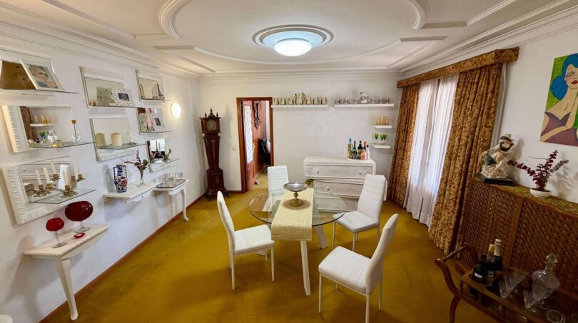Elegant dining room of the retro villa in Porto Cristo with stucco ceiling, glass table and yellow carpet.