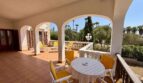 Covered terrace of the villa in Porto Cristo with arch construction, yellow seating furniture and view of palms.