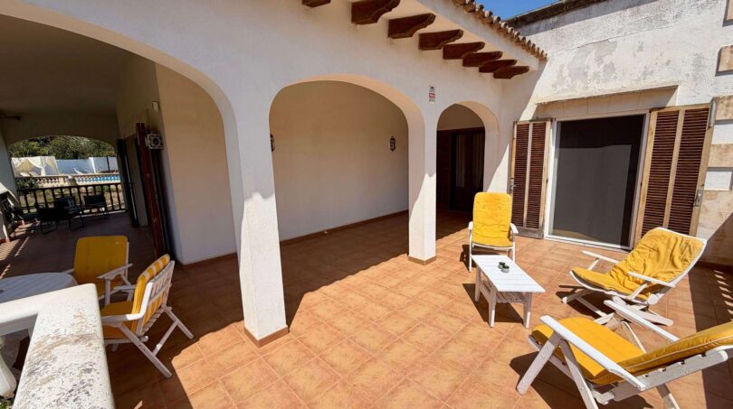Sunny terrace of the retro villa in Porto Cristo with sun loungers, round arches and terracotta tiles.