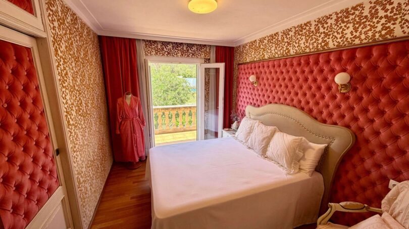 Elegant bedroom with red velvet upholstery, parquet floor and balcony with garden view in Retro-Villa Porto Cristo.